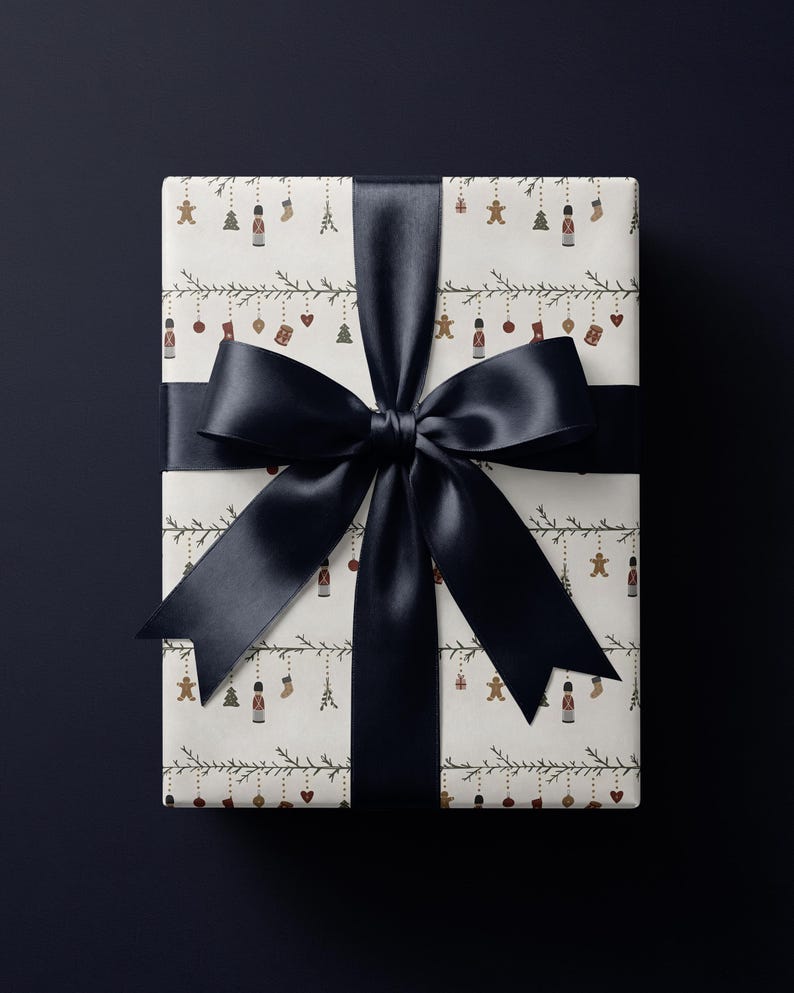 May include: A rectangular gift box wrapped in off-white paper featuring a repeating pattern of small holiday icons including nutcrackers, gingerbread men, stockings, and ornaments hanging from thin green garlands, tied with a wide black satin ribbon.