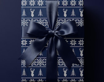 May include: A rectangular gift box wrapped in dark blue paper featuring a white repeating pattern of deer, pine trees, and snowflakes. The package is tied with a wide, dark blue satin ribbon that is tied into a large, centered bow on the front.