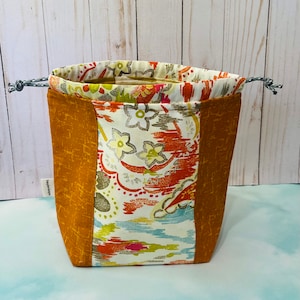 Könnte beinhalten: Eine Kordeltasche mit einem floralen Muster in Orange-, Rosa-, Grün- und Blautönen. Die Tasche hat ein braunes Stofffutter und einen weißen Kordelzug.