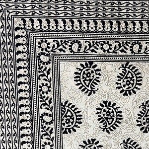 May include: A white fabric with a black paisley pattern. The fabric has a border with a repeating pattern of black and white.