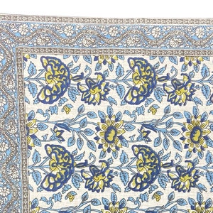 May include: A white cotton square table runner with a blue and yellow floral pattern. The runner has a decorative border with a blue and gray floral design.