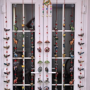 May include: A set of eight colourful hanging decorations with various animal and umbrella designs. Each decoration features a string of beads with small bells at the bottom. The decorations are hung on a white door with glass panels.
