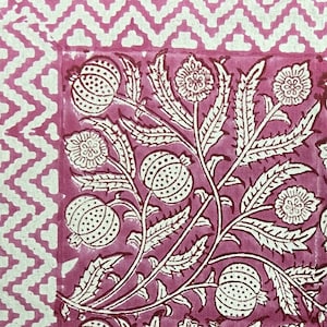 Puede incluir: Una tela rosa con un patrón floral blanco. El patrón presenta flores y hojas estilizadas con un diseño repetitivo. La tela tiene un borde a cuadros rosa y blanco.