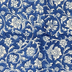 Op de afbeelding: Een blauwe en witte stof met een bloemenpatroon. De stof heeft een witte rand met een geometrisch patroon.