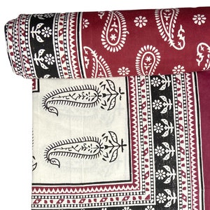 May include: A maroon and white cotton fabric with a paisley print. The fabric is folded and rolled up.