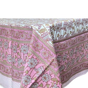 May include: Pink tablecloth with a floral pattern in shades of pink, brown, and white. The tablecloth has a border with a geometric design.