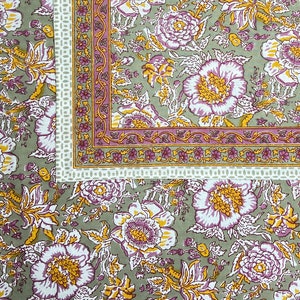 May include: A green fabric with a floral pattern in shades of pink, white, and yellow. The fabric has a border with a white, pink, and yellow pattern.