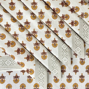 May include: Set of six white cotton napkins with a gray and white border and a brown and yellow floral pattern. The napkins are folded in a triangle shape.
