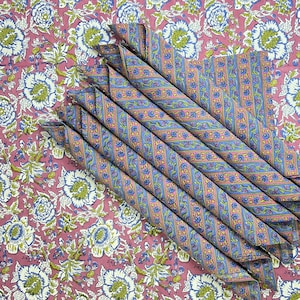 May include: A stack of blue and pink striped napkins folded on a pink floral fabric background.