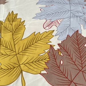 May include: A white fabric with a pattern of colourful leaves. The leaves are in shades of red, yellow, blue, and brown. The leaves are arranged in a random pattern.