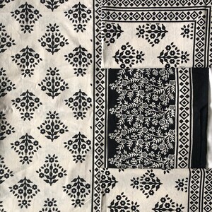 Puede incluir: Un conjunto de tela de algodón blanco y negro con un patrón floral. La tela tiene un borde con un diseño geométrico.