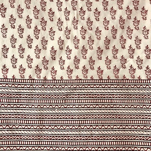 May include: Cream-colored fabric with a repeating pattern of dark red floral motifs. The bottom section features horizontal bands of alternating geometric designs in dark red and white. The fabric has a textured appearance.