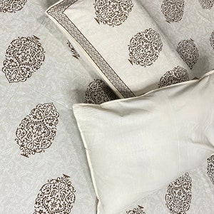 May include: Two white pillowcases with brown floral patterns. The pillowcases are on a white bed sheet with a similar brown floral pattern.
