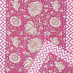 May include: Pink fabric with a white floral pattern. The fabric has a white and pink zig-zag border.