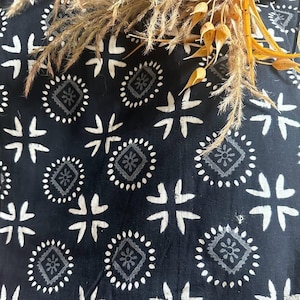 May include: Black fabric with a white geometric pattern. The pattern features repeating circles with a square in the centre and a small flower design inside the square. The fabric has a textured, hand-woven look.