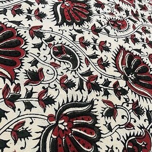 Puede incluir: Una tela blanca con un patrón repetido de diseños florales negros y rojos. Las flores son estilizadas y tienen una apariencia de paisley.