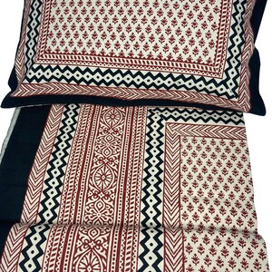 Puede incluir: Un juego de cama de algod&oacute;n con estampado negro y rojo con una funda de almohada. La ropa de cama presenta un dise&ntilde;o geom&eacute;trico con detalles en negro, blanco y rojo.