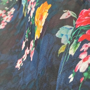 Puede incluir: Primer plano de una tela azul oscuro con estampado floral. Las flores son en tonos de rosa, rojo, amarillo y verde.