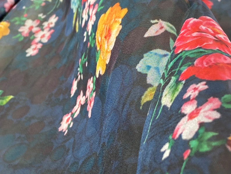 Puede incluir: Primer plano de una tela azul oscuro con estampado floral. Las flores son en tonos de rosa, rojo, amarillo y verde.