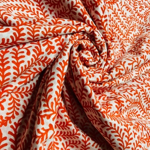 Puede incluir: Tela blanca con un patrón floral naranja repetido. La tela está doblada y retorcida, mostrando el patrón desde diferentes ángulos.