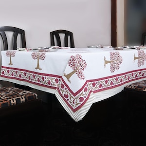 May include: White tablecloth with a red and gold floral border and tree design. The tablecloth is laid on a table with four chairs.