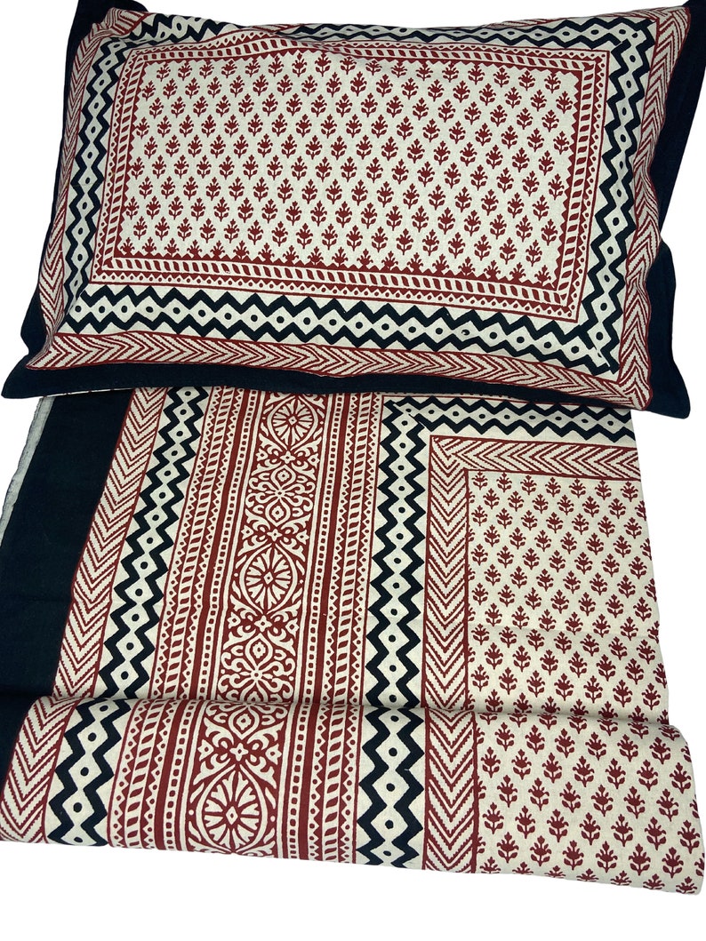 Puede incluir: Un juego de cama de algod&oacute;n con estampado negro y rojo con una funda de almohada. La ropa de cama presenta un dise&ntilde;o geom&eacute;trico con detalles en negro, blanco y rojo.