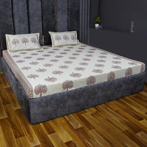 May include: A white bed with a brown tree print bed sheet and two matching pillowcases. The bed has a dark gray headboard and footboard and is sitting on a wooden floor.