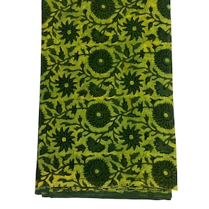 Può includere: Un tessuto verde con un motivo floreale giallo. Il tessuto è piegato e ha una texture liscia.