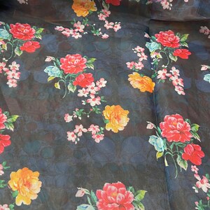 Puede incluir: Una tela transparente azul oscuro con estampado floral. Las flores son rojas, naranjas, amarillas, rosas y azules. La tela tiene un sutil patr&oacute;n de lunares.