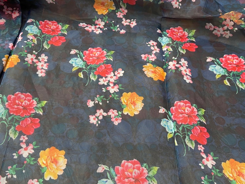 Puede incluir: Una tela transparente azul oscuro con estampado floral. Las flores son rojas, naranjas, amarillas, rosas y azules. La tela tiene un sutil patr&oacute;n de lunares.