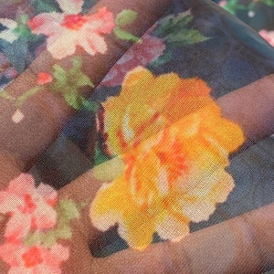 Puede incluir: Primer plano de una tela transparente con estampado floral. La tela presenta una gran flor amarilla con acentos naranjas, rodeada de flores m&aacute;s peque&ntilde;as de color rosa y blanco.