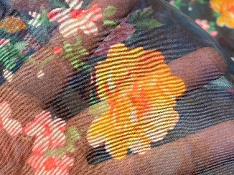 Puede incluir: Primer plano de una tela transparente con estampado floral. La tela presenta una gran flor amarilla con acentos naranjas, rodeada de flores m&aacute;s peque&ntilde;as de color rosa y blanco.