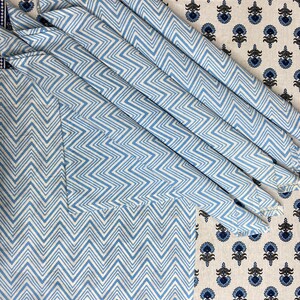 May include: Set of blue and white chevron patterned napkins. The napkins are folded and stacked on a white background with a blue floral pattern.