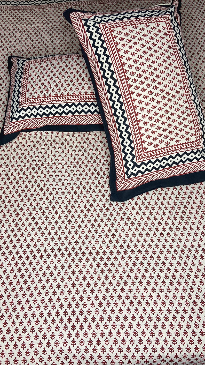 Puede incluir: Dos fundas de almohada blancas con un patr&oacute;n floral rojo y negro. Las fundas de almohada tienen un borde negro con un dise&ntilde;o geom&eacute;trico.