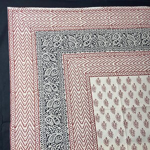 Puede incluir: Una tela de algodón blanca con un estampado paisley negro y rojo. La tela tiene un borde con un patrón geométrico.