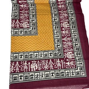 May include: A maroon cotton fabric with a yellow and white geometric pattern. The fabric has a border of black and white stylized figures.
