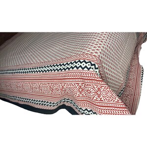 Puede incluir: Una s&aacute;bana de cama de algod&oacute;n blanco con un borde geom&eacute;trico rojo y negro. La s&aacute;bana tiene un peque&ntilde;o patr&oacute;n floral en toda su superficie.