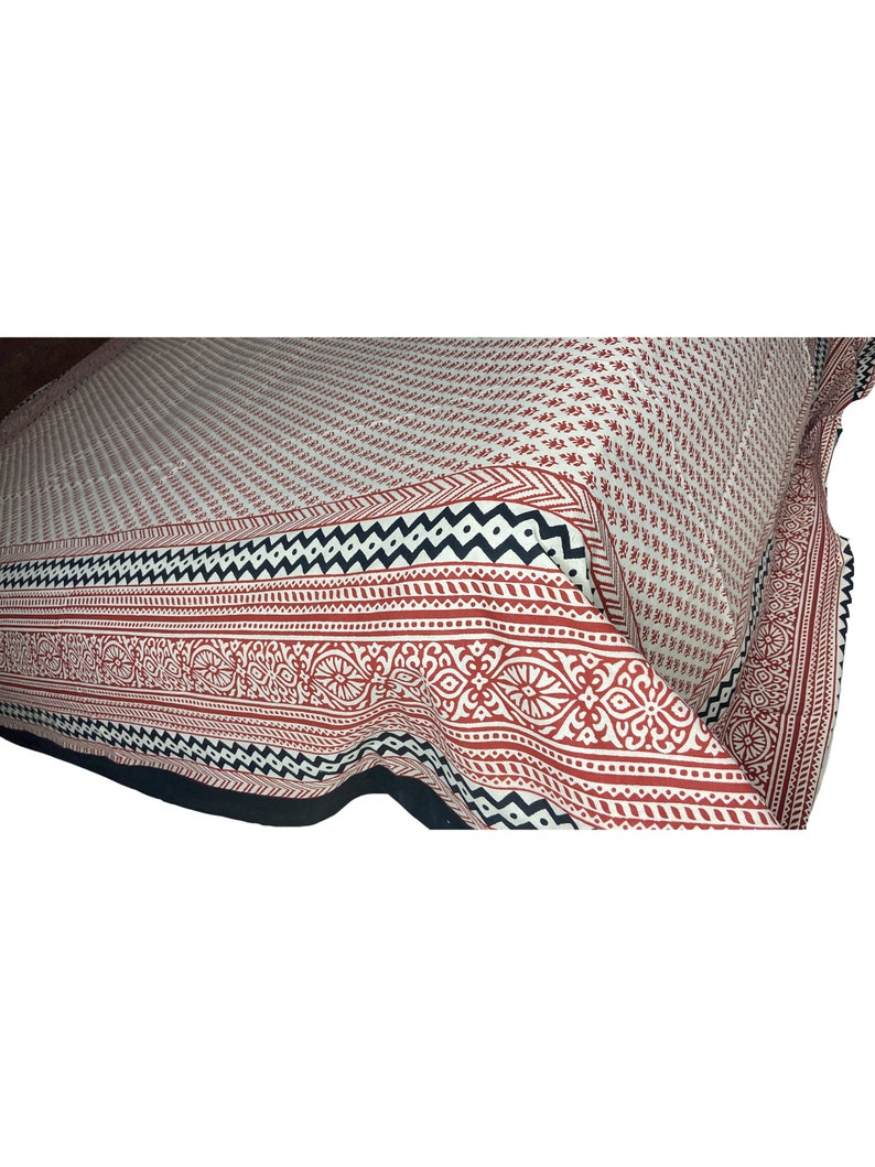 Puede incluir: Una s&aacute;bana de cama de algod&oacute;n blanco con un borde geom&eacute;trico rojo y negro. La s&aacute;bana tiene un peque&ntilde;o patr&oacute;n floral en toda su superficie.