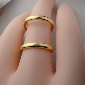 May include: Two gold wedding bands stacked on a finger. The bands are simple and smooth.