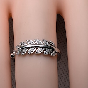May include: A silver ring with a leaf design, set with small, clear gemstones. The ring is shaped like a delicate branch with multiple leaves, each with sparkling stones. The ring is worn on a finger.