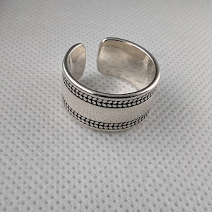 May include: A silver ring with a textured band. The band has a row of small dots around the top and bottom edges.