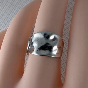 May include: A silver ring with a hammered, textured finish. The ring is wide and has a slightly curved shape.