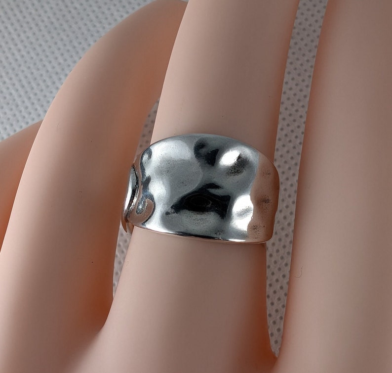 May include: A silver ring with a hammered, textured finish. The ring is wide and has a slightly curved shape.