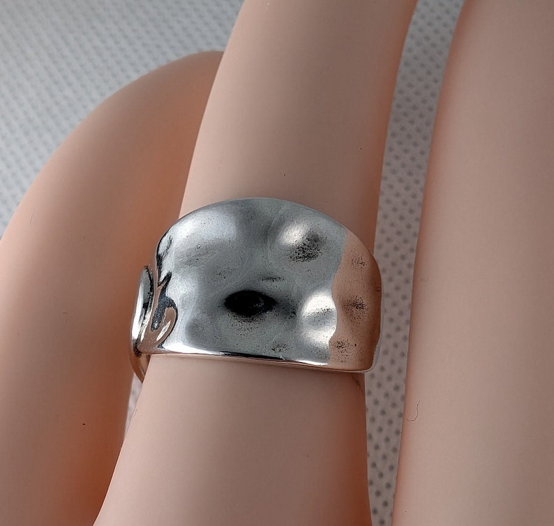 May include: A silver ring with a hammered, textured surface. The ring is wide and has a rounded shape.