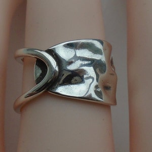 May include: A silver ring with a textured, hammered design. The ring has a unique, open band that wraps around the finger.