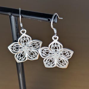 May include: A pair of silver flower-shaped dangle earrings with intricate filigree details.