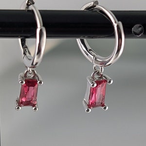 May include: A pair of silver hoop earrings with a dangling rectangular red gemstone.