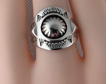 May include: A silver ring with a circular design featuring a central sunburst motif surrounded by a geometric pattern.