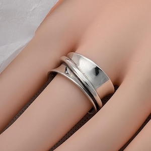 May include: A silver spinning ring with a wide band and a curved design. The ring is worn on a finger.
