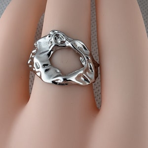 May include: A silver ring with an abstract, organic design. The ring is open in the centre, creating a circular opening.